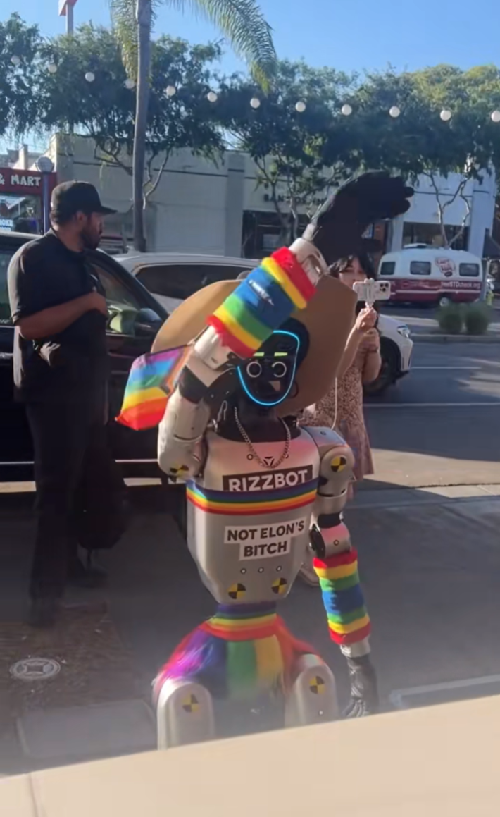 Rizzbot covered in rainbow flags waving at a bar.