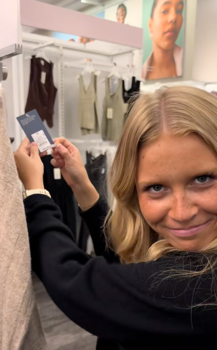 TikToker peeling the price sticker off a Target sweater to reveal a lower price. She is making an annoyed face at the camera.