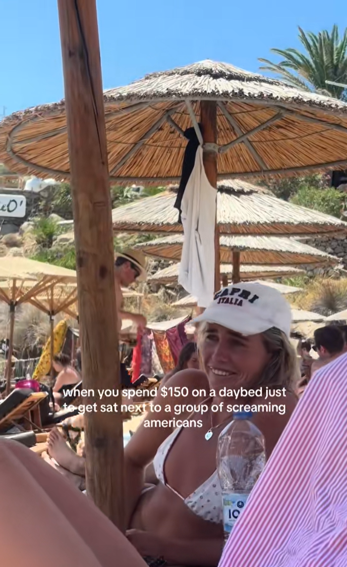 Women hanging out in beach loungers and making fun of the group of Americans behind them.