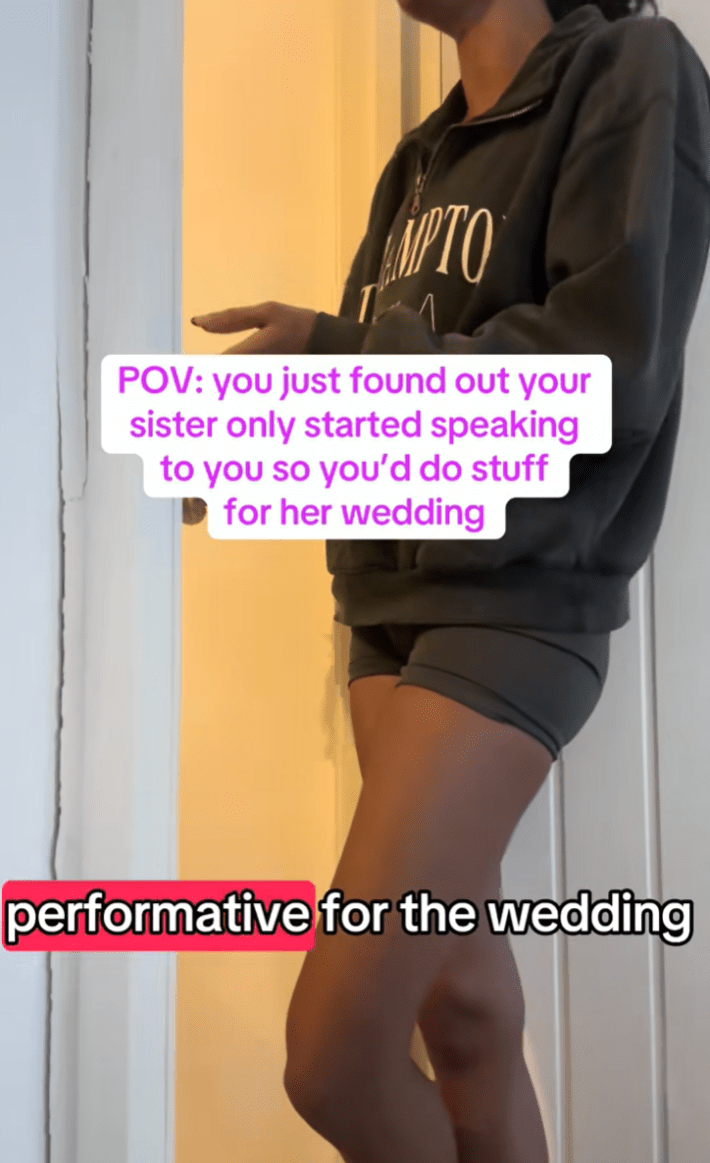 Woman leaning in her bedroom doorframe in a protective posture, gesturing with one hand as she talks to her family in the other room.