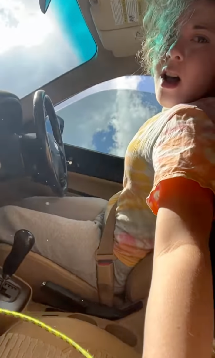 Woman grabbing her phone after her car crashed and flipped on its side.