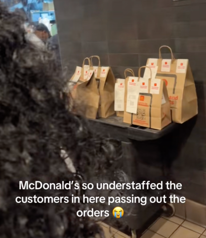 @styledbymoonkk wrote in onscreen text, “McDonalds so understaffed the customers in here passing out the orders  😭." Customer passing out orders in crowded McDonalds