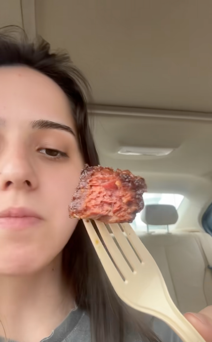 A woman sitting in a car showing a "steak bite" with a bite taken out of it. It does not look like steak on the inside.