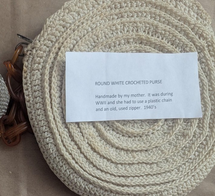 vintage purse with note that reads, "round white crocheted purse. handmade by my mother, it was during WWII and she had to use a plastic chain and an old, used zipper. 1940s."