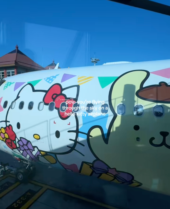exterior of Hello Kitty jet with characters painted on the side of it and onscreen text “POV: you’re flying through the sky on a Hello Kitty plane.”