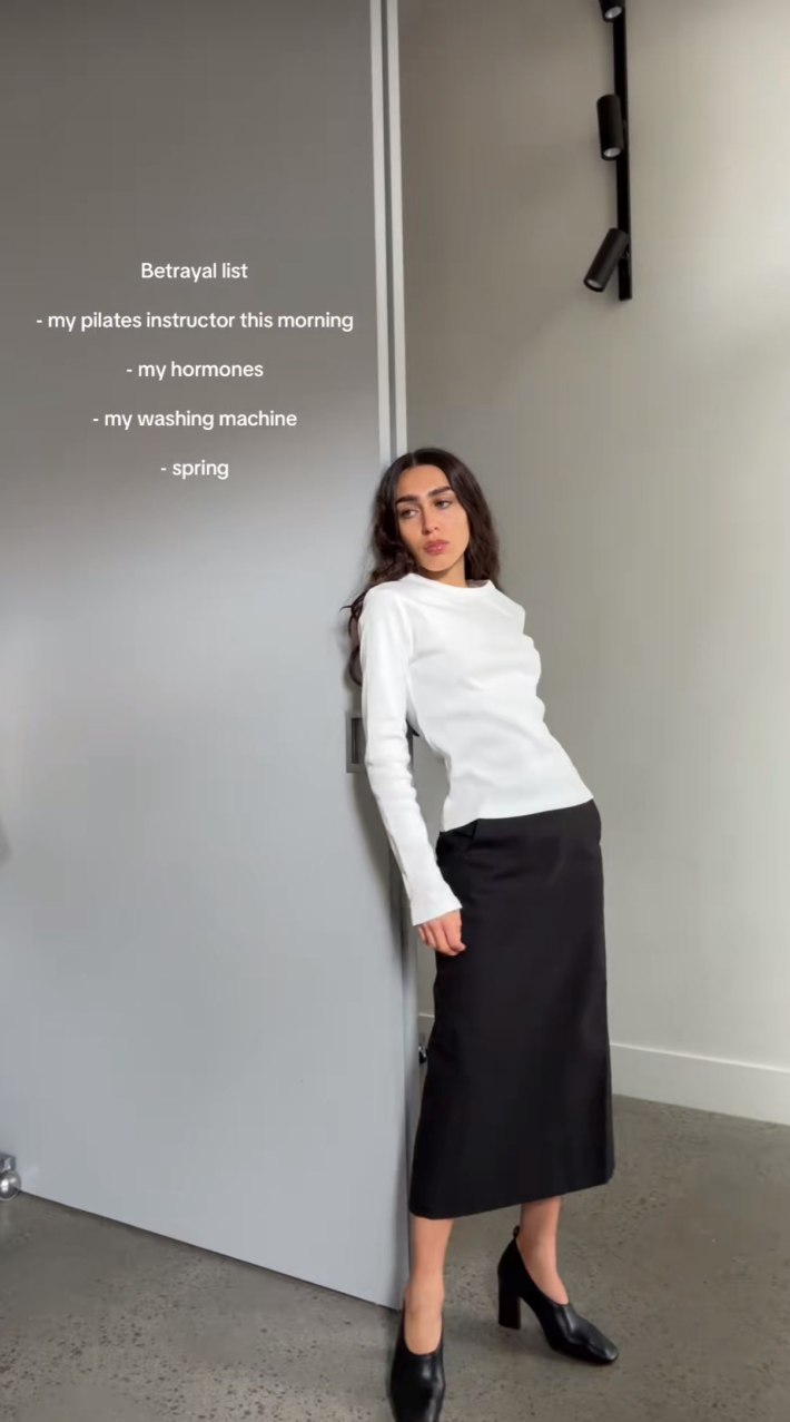 A woman posing in a white top and black skirt, her "betrayal list" on the screen.