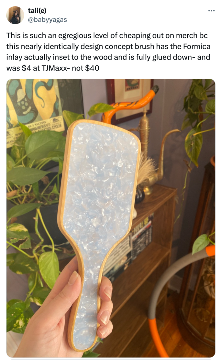 Tweet that reads, "This is such an egregious level of cheaping out on merch bc this nearly identically design concept brush has the Formica inlay actually inset to the wood and is fully glued down- and was $4 at TJMaxx- not $40" with a photo of the brush.
