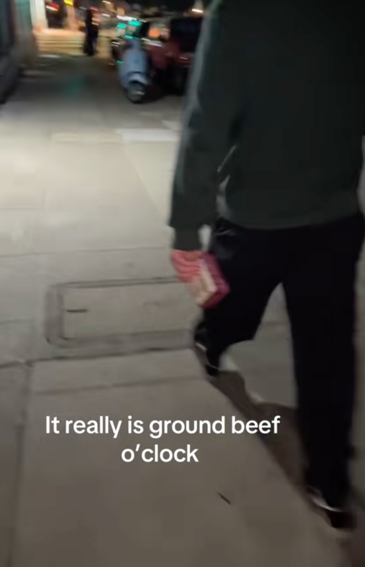 man walking on the street holding container of ground beef with onscreen text: it really is ground beef o'clock