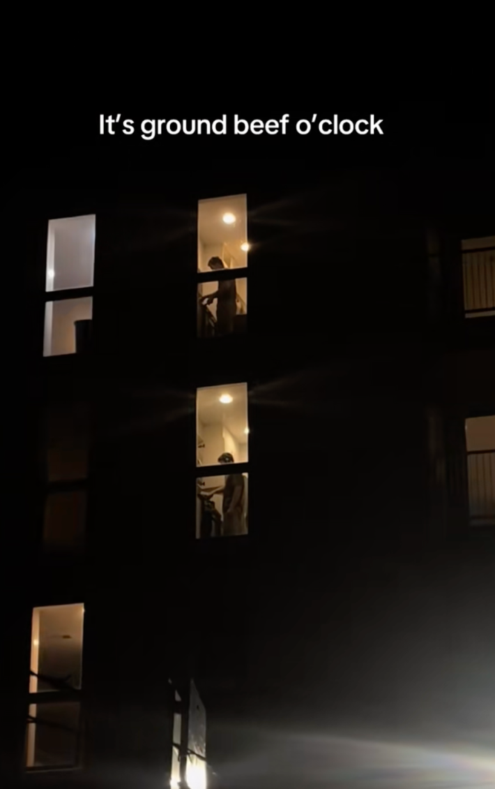 shot from the street, man cooking inside his apartment with onscreen text "it's ground beef o'clock."
