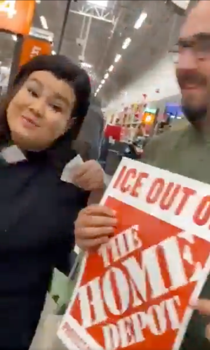 A man and woman posing at self-checkout with a "ICE out of the Home Depot."
