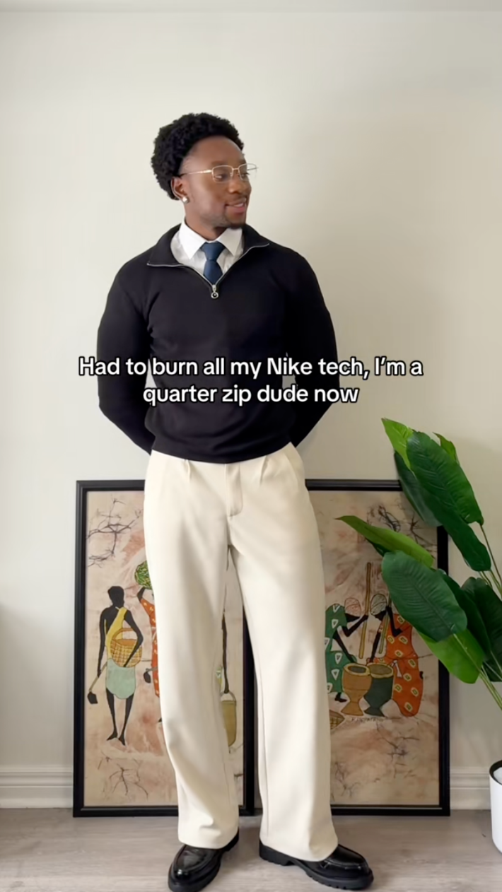 A Black man dressed up in a quarter-zip sweater and chinos.