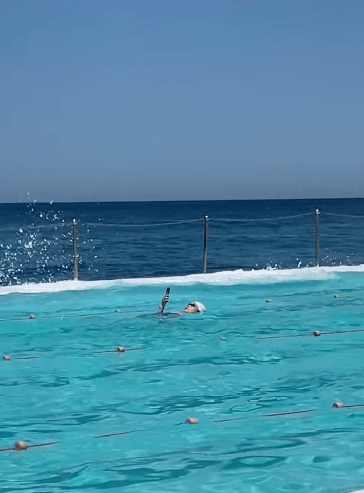 @browncardigan/Instagram swimming laps back stroke in public pool while looking at phone and taking selfie