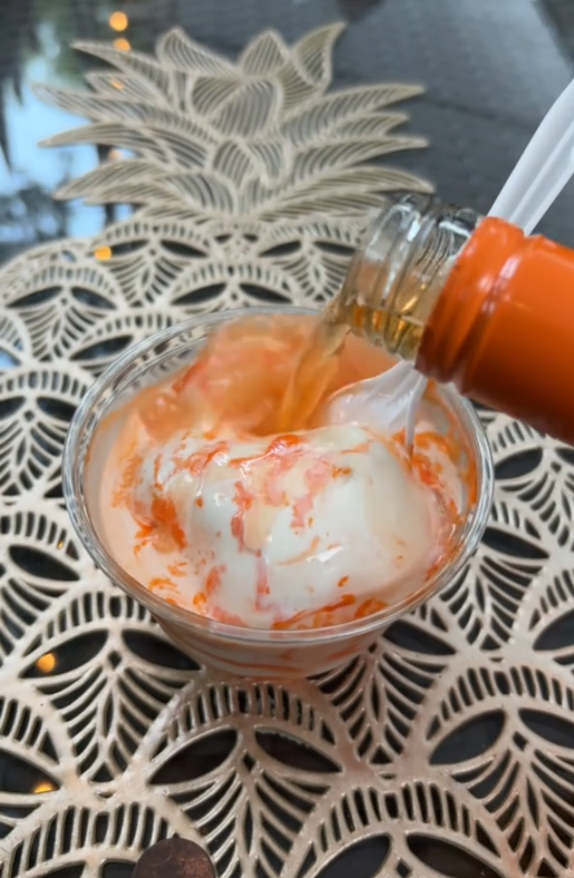 Video of someone pouring orange wine into a plastic cup containing scoops of vanilla ice cream.
