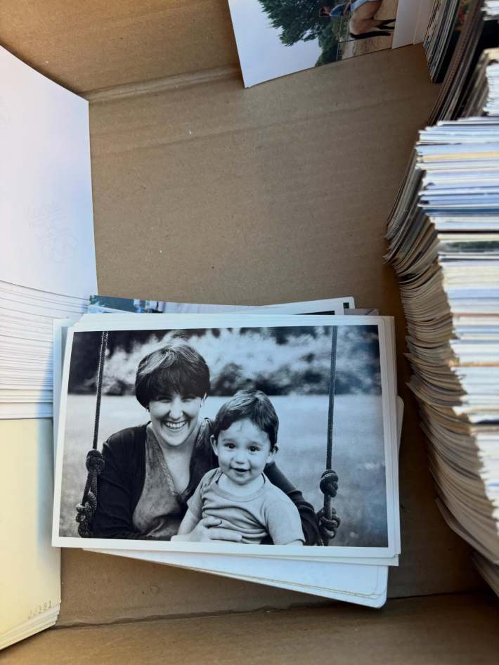 Black and white photo of a smiling woman and her son. The photo is in a cardboard box and surrounded by stacks of other photos.