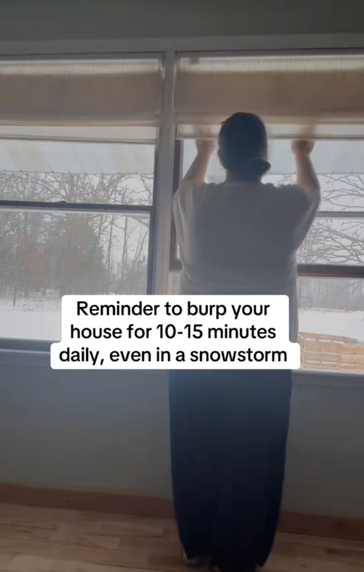 @fasciacodes/TikTok woman opening a window with onscreen text: reminder to burp your house for 10-15 minutes daily, even in a snowstorm
