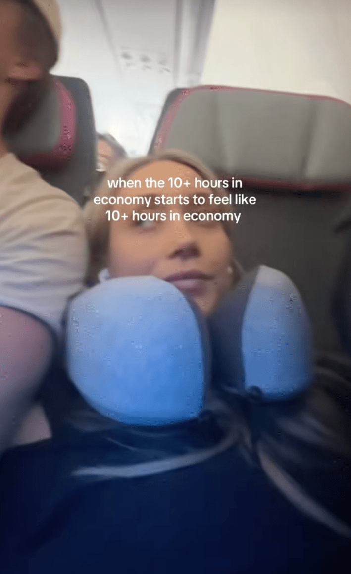 Fast (29), seated in a window seat beside her husband, stretched her legs up the wall of the plane beneath onscreen text that read, “when the 10+ hours in economy starts to feel like 10+ hours in economy.”