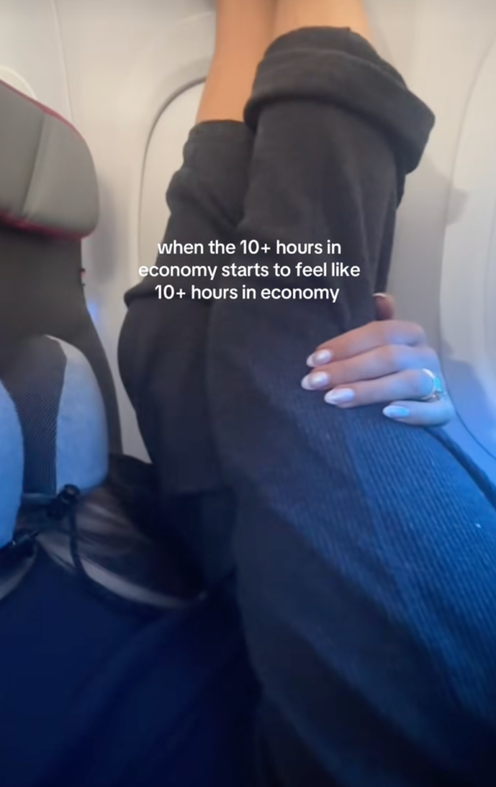 Fast (29), seated in a window seat beside her husband, stretched her legs up the wall of the plane beneath onscreen text that read, “when the 10+ hours in economy starts to feel like 10+ hours in economy.”