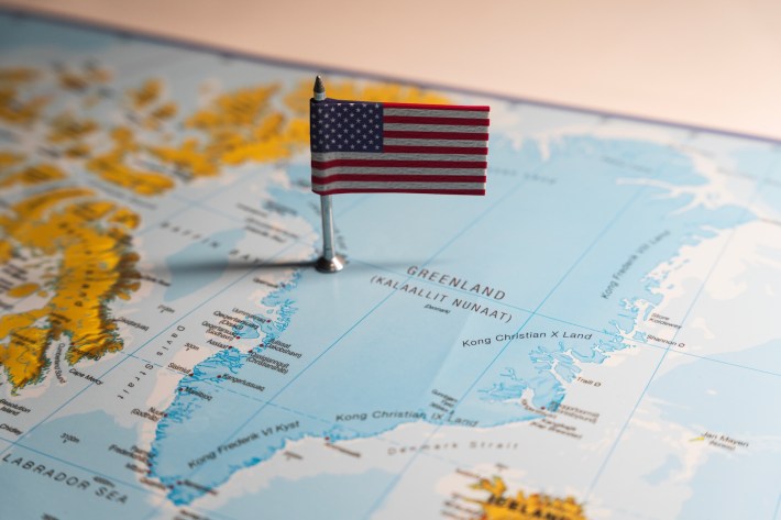 An American flag pin placed on Greenland on a world map, highlighting the geopolitical relationship and potential US interests in the Arctic region.