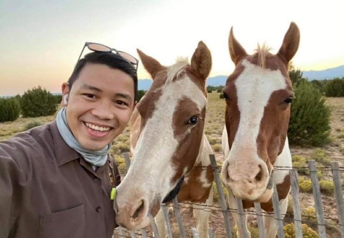 A UPS driver posing with two white and tan horses in a field.