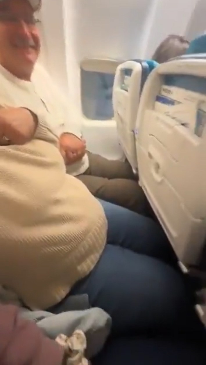 An older couple on an airplane, their knees literally under the seats in front of them due to a lack of leg room.