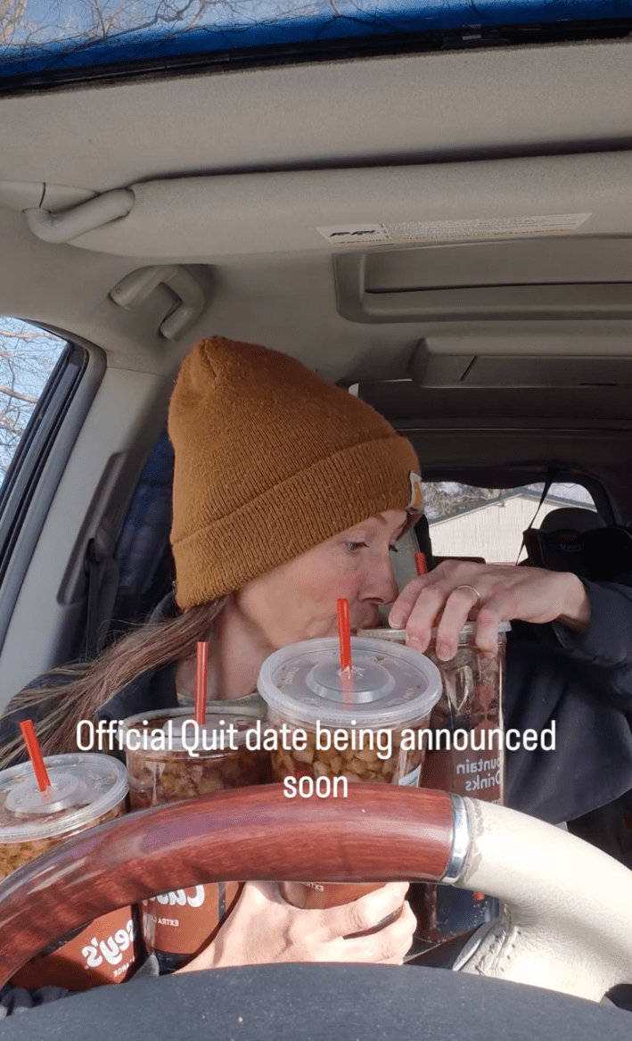 A woman in a brown beanie sitting in her car, four 44-oz plastic cups of diet soda in her arms as she drinks from one of them. Text overlay reads, "Official Quit date being announced soon."