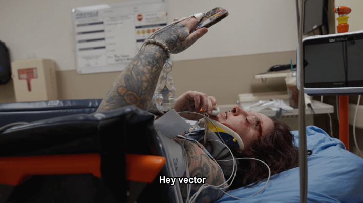 woman in the hospital holds up the "friend" necklace and says "Hey vector"