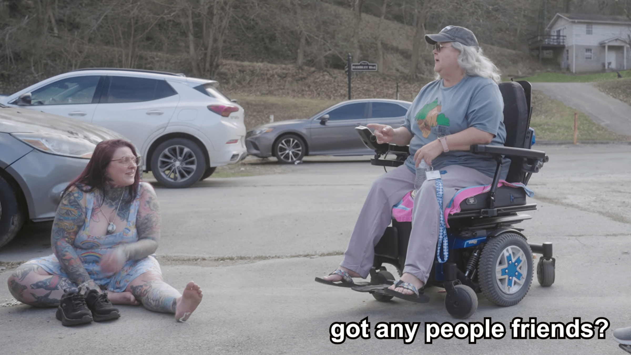 a woman in a wheelchair asks another woman wearing an ai necklace, "got any people friends?"
