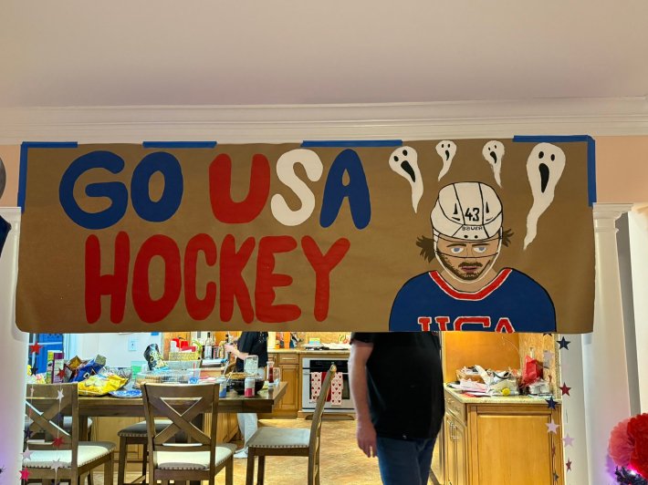 A photo of a hand-painted "GO USA HOCKEY" sign hanging in someone's house, Quinn Hughes painted on one side surrounded by white ghosts, their mouths open wide.