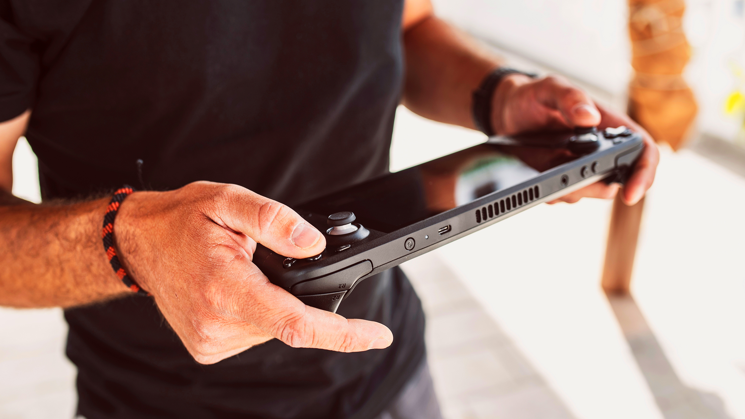 Man's hands holding Válvuve Steam Deck handheld game console.