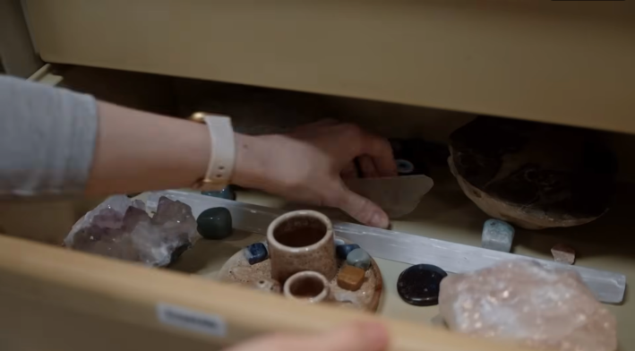 An open drawer filled with crystals, a woman's arm reaching in to grab one.