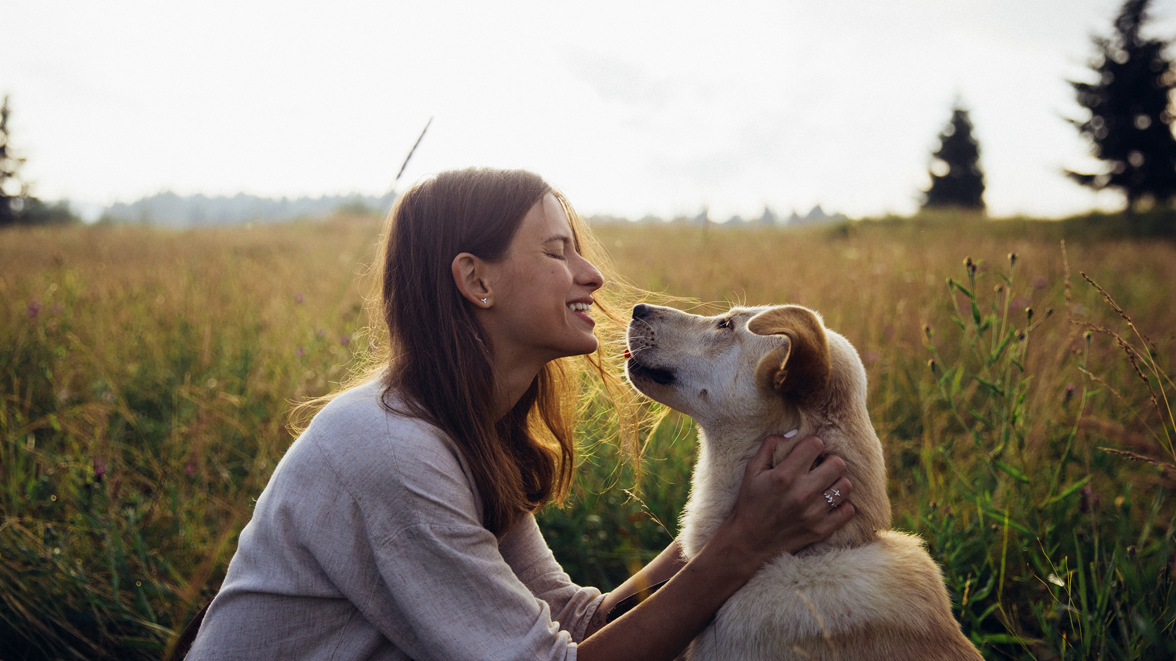 Young woman smiling with her blonde dog, smiling into its face against a straw field background.