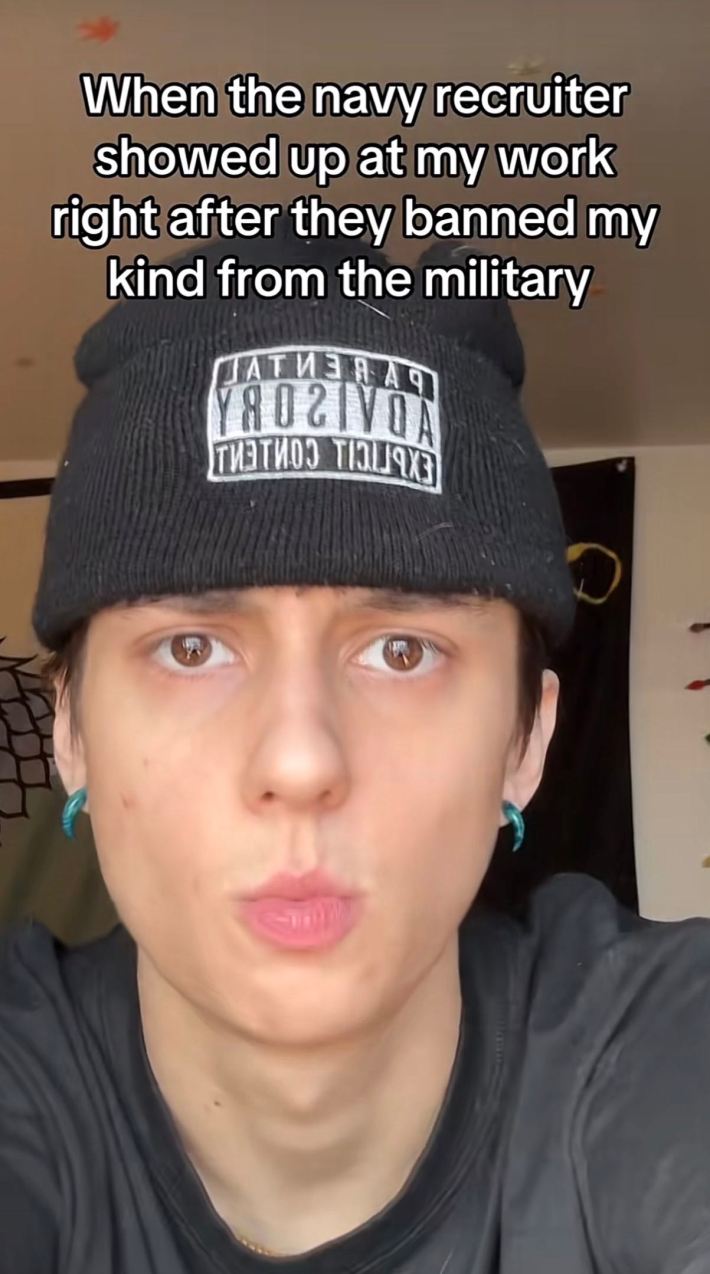 A person in a "parental advisory" beanie staring at the camera. Text overlay reads, "When the navy recruiter showed up at my work right after they banned my kind from the military."