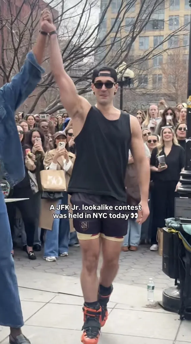 Man in casual gym clothes and roller blades standing in front of a crowd of people with someone else raising his arm in the air in victory.