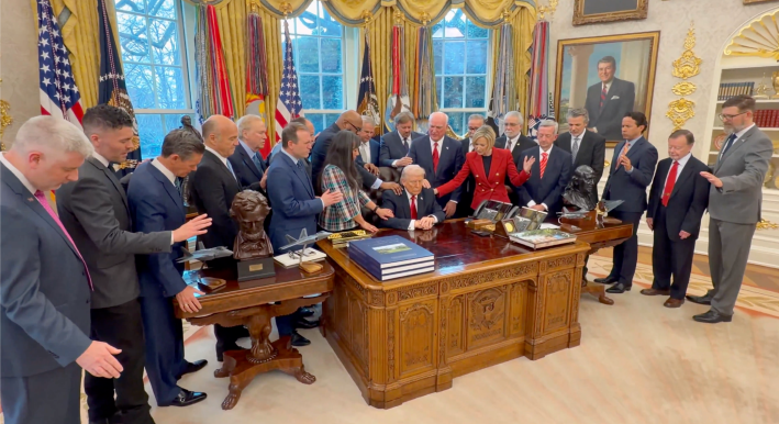 A crowd of people with hands and arms outstretched to pray over Trump like he's a religious prophet.