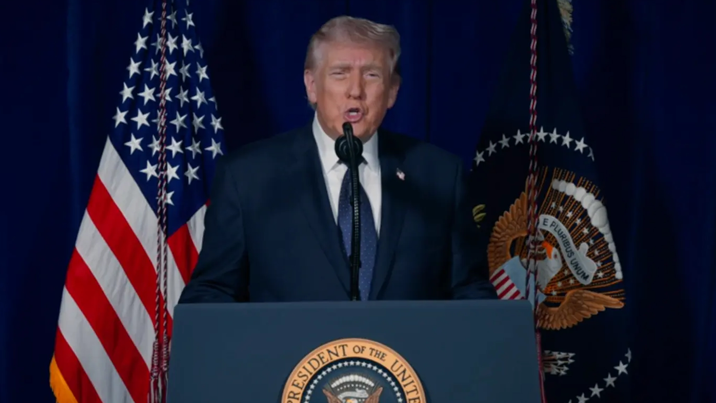 President Donald Trump standing at a presidential podium speaking to the camera.