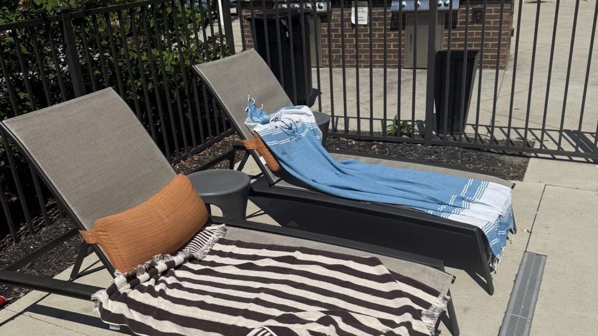 Two empty pool lounge chairs with towels on them by a fence