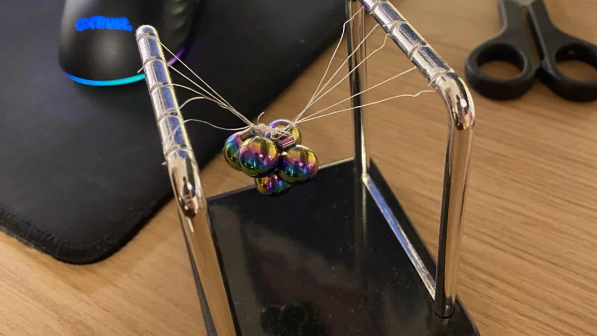 Newton's Cradle with tangled wires and clustered metal balls on a desk